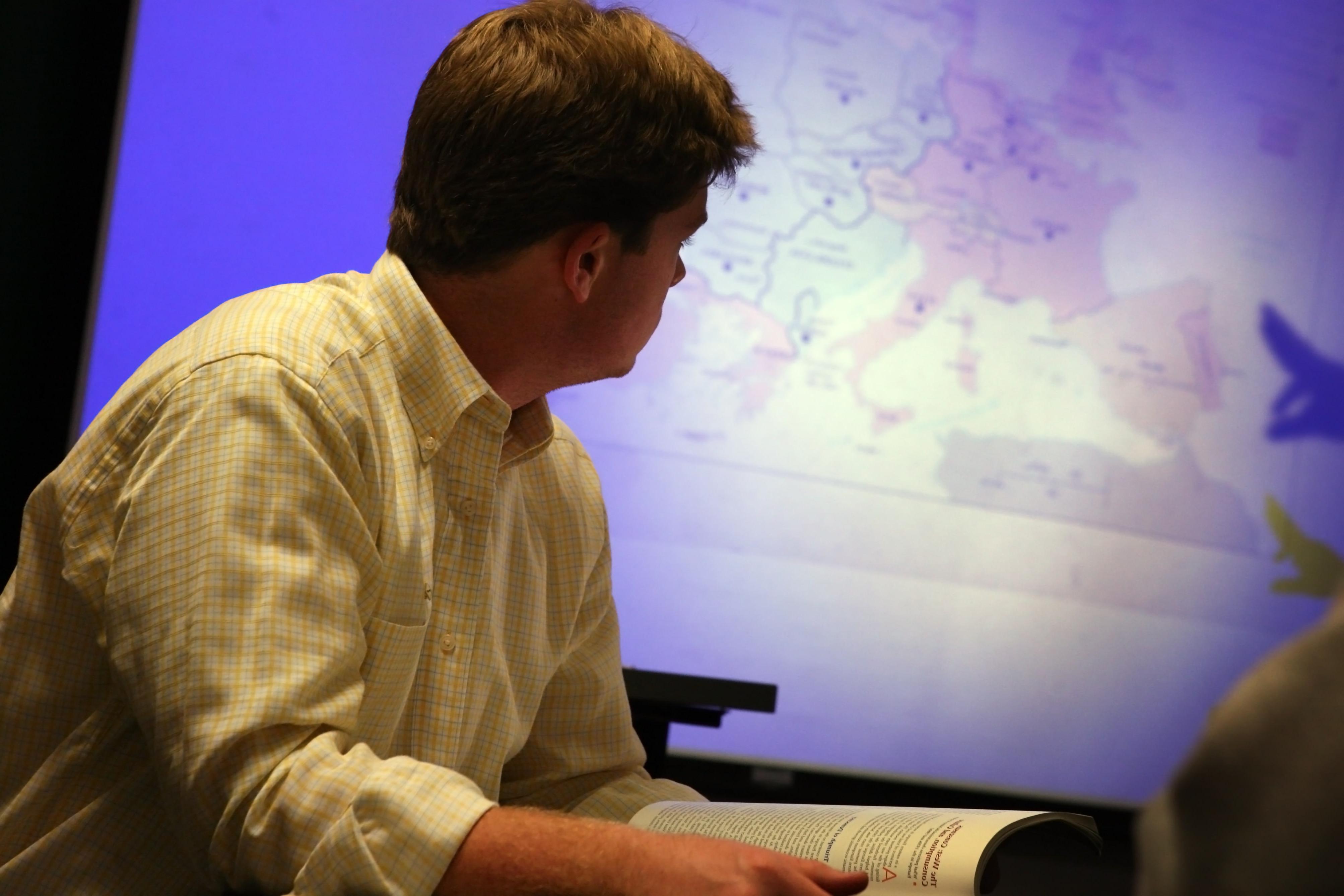 A student studies a map projected on a large screen in a classroom.